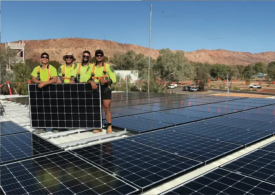 A Group of Men Are Standing on Top of A Roof Holding Solar Panels — Eco Sparks Solar & Electrical Contractors in Berrimah, NT