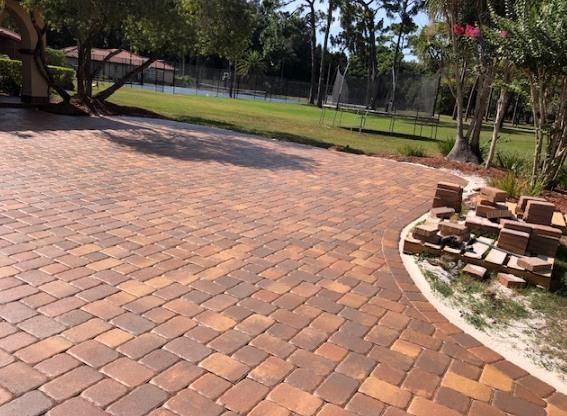 a brick driveway with a fountain in the middle and a tennis court in the background .