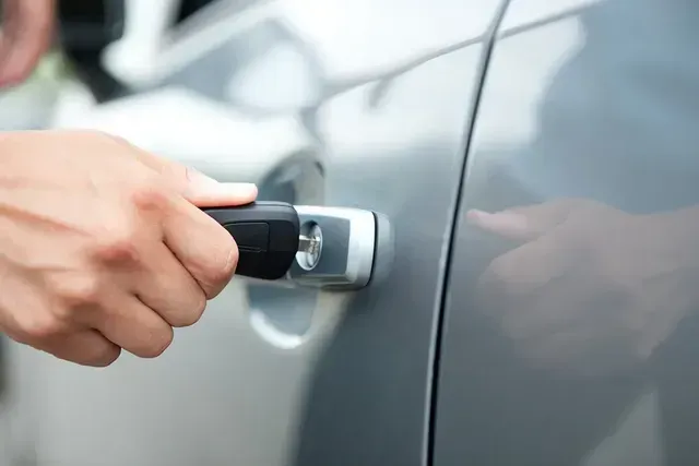 A person is opening the door of a car with a key.
