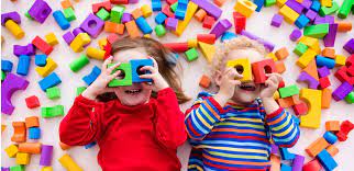 A boy and a girl are laying on the floor playing with colorful blocks.