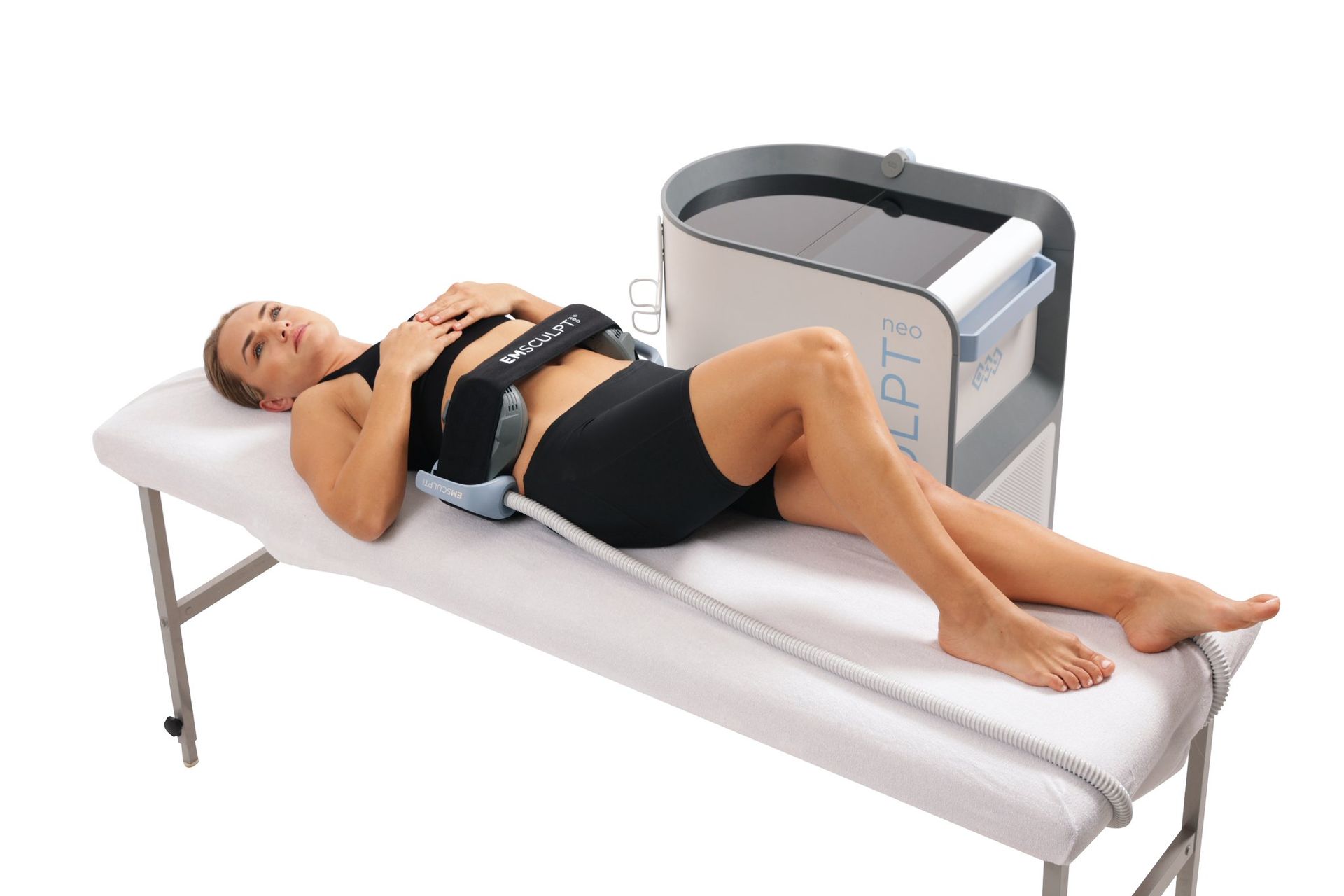 Woman lying on a treatment table with a medical therapy device beside her, wearing a belt around her waist.