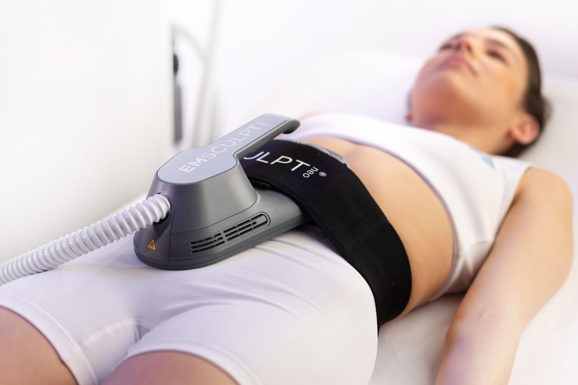 Woman receiving body contouring treatment with a handheld device strapped over her abdomen