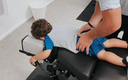 Child on an exam table during a chiropractic adjustment, with a practitioner supporting their legs.