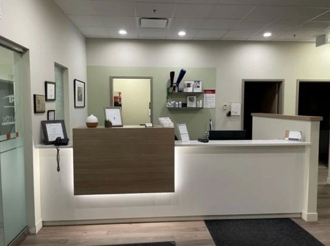 Modern office reception desk with white and wood paneling, shelving, and hallway openings behind it