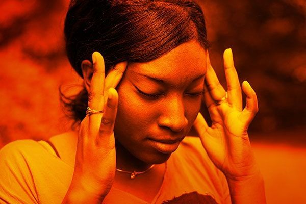 Woman holding her temples with eyes closed against an orange background, looking stressed