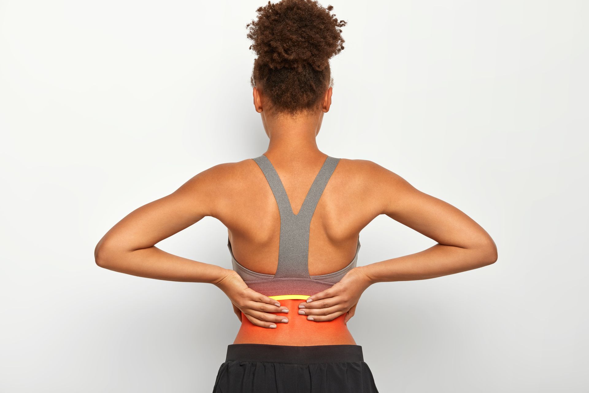 Person holding lower back with red-highlighted pain area, viewed from behind in a gray sports bra.