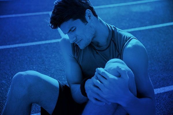 Blue-tinted athlete sitting on a track, holding their head in exhaustion or distress
