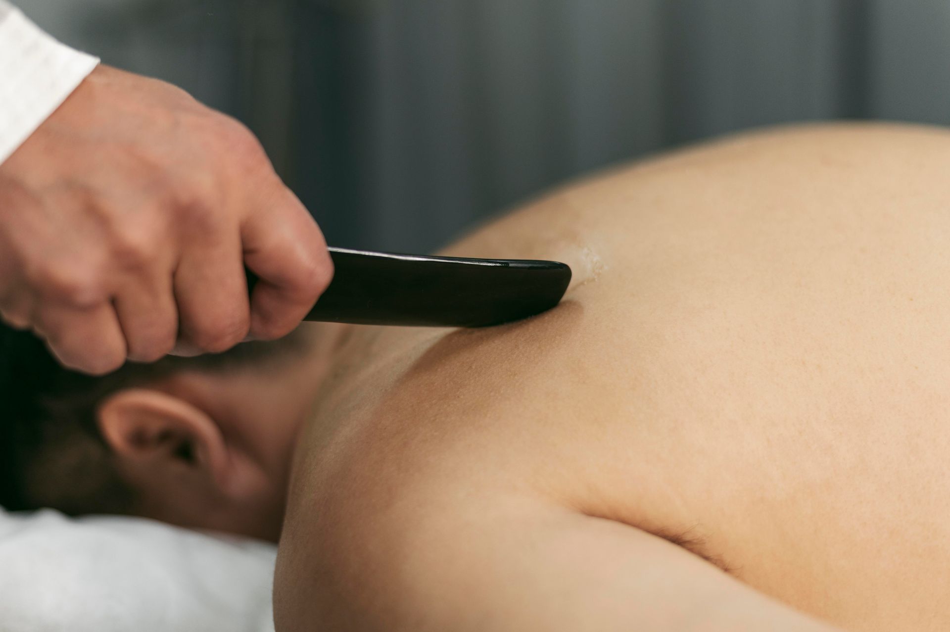 Hand holding a black gua sha tool on a person’s bare upper back during a massage