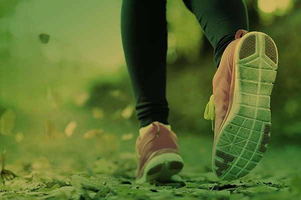 Close-up of a runner’s feet in pink shoes jogging on a green path outdoors