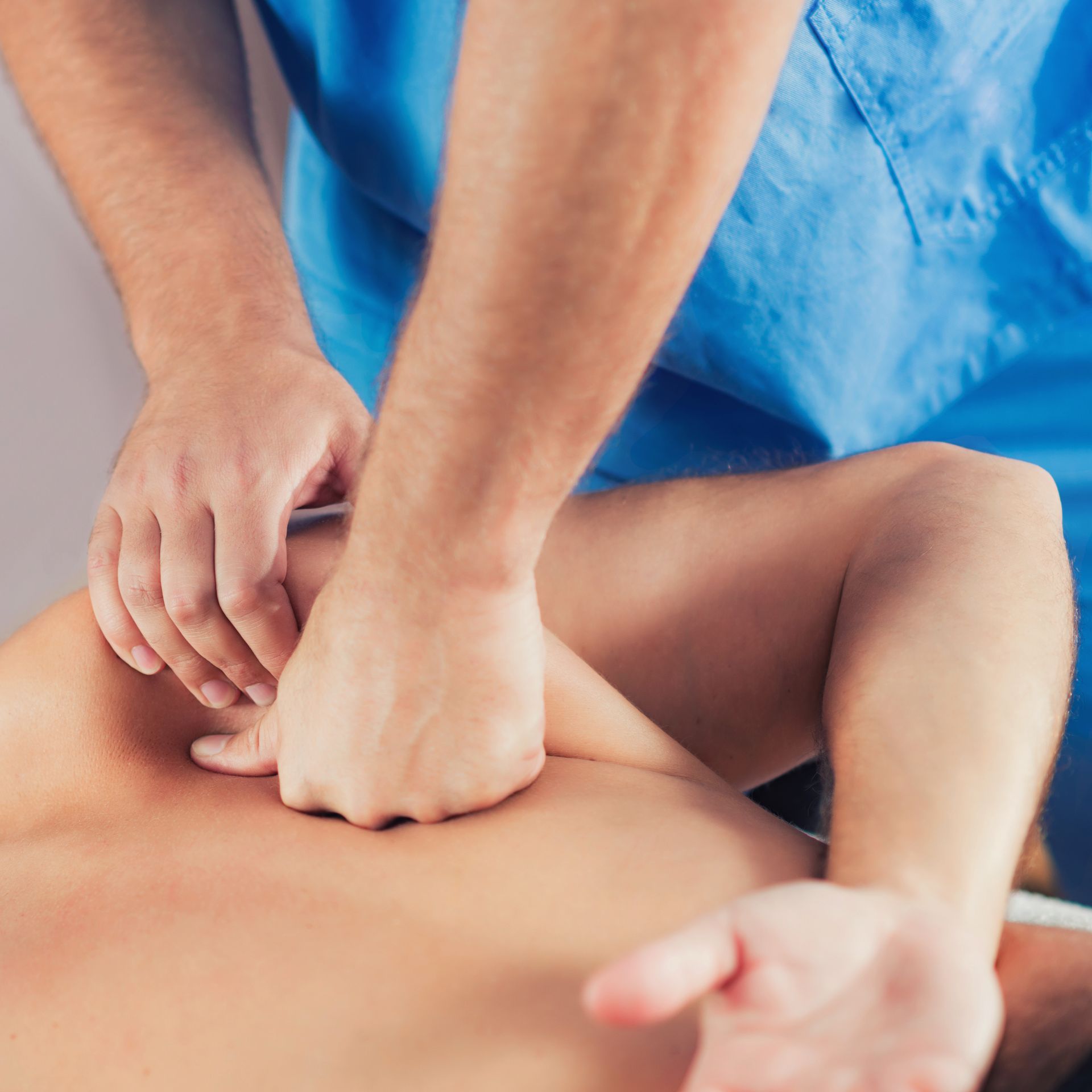 Hands pressing a person’s back during a massage, with blue fabric in the background