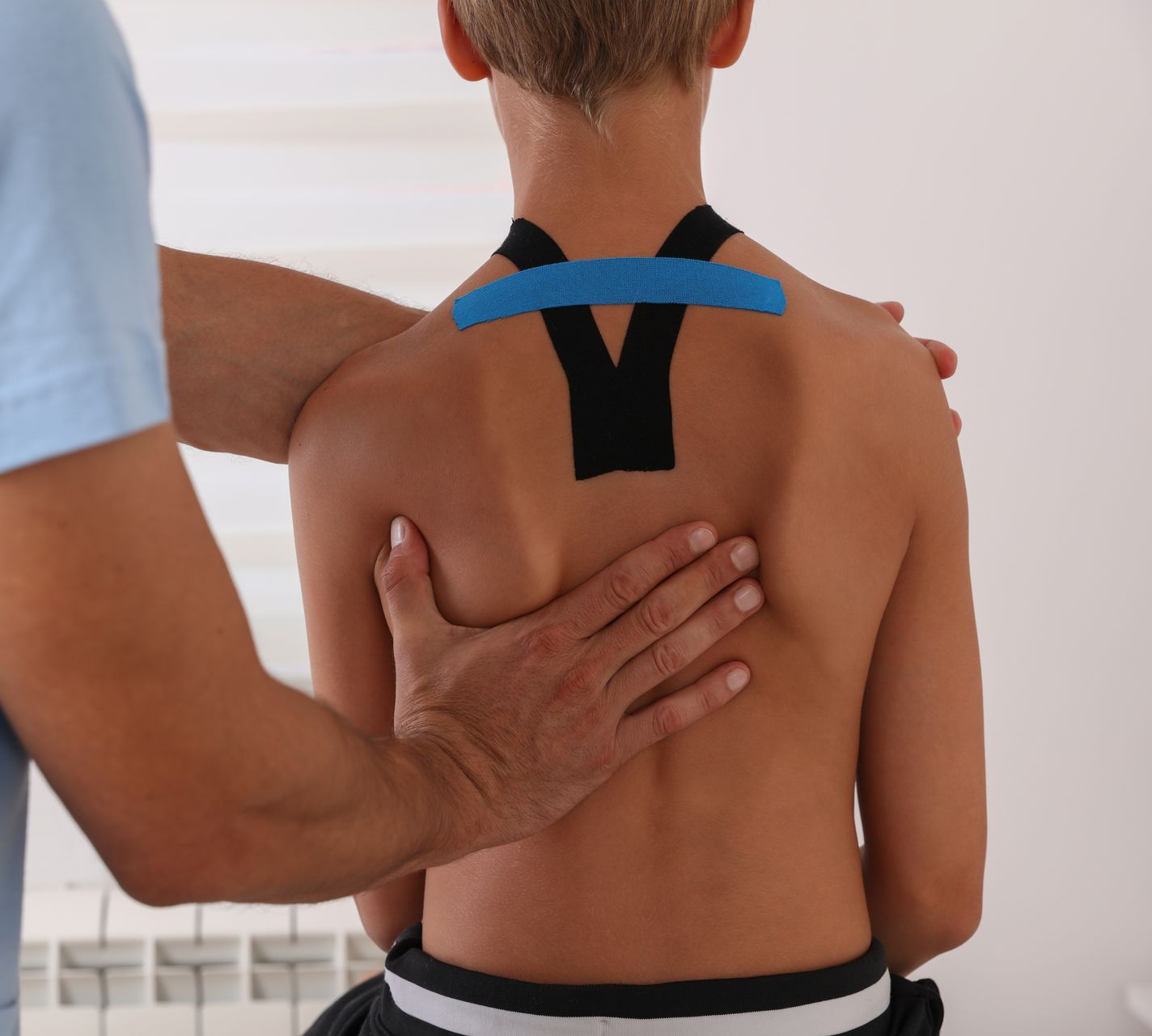Physical therapist applying kinesiology tape to a boy’s upper back and shoulder