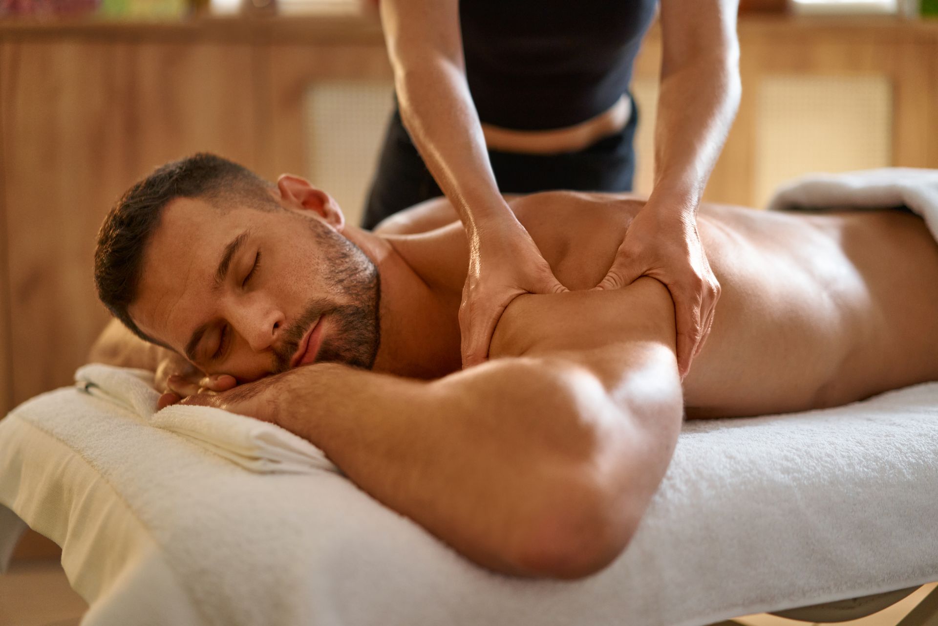 Man receiving a shoulder massage on a spa table, eyes closed, in a warm indoor setting