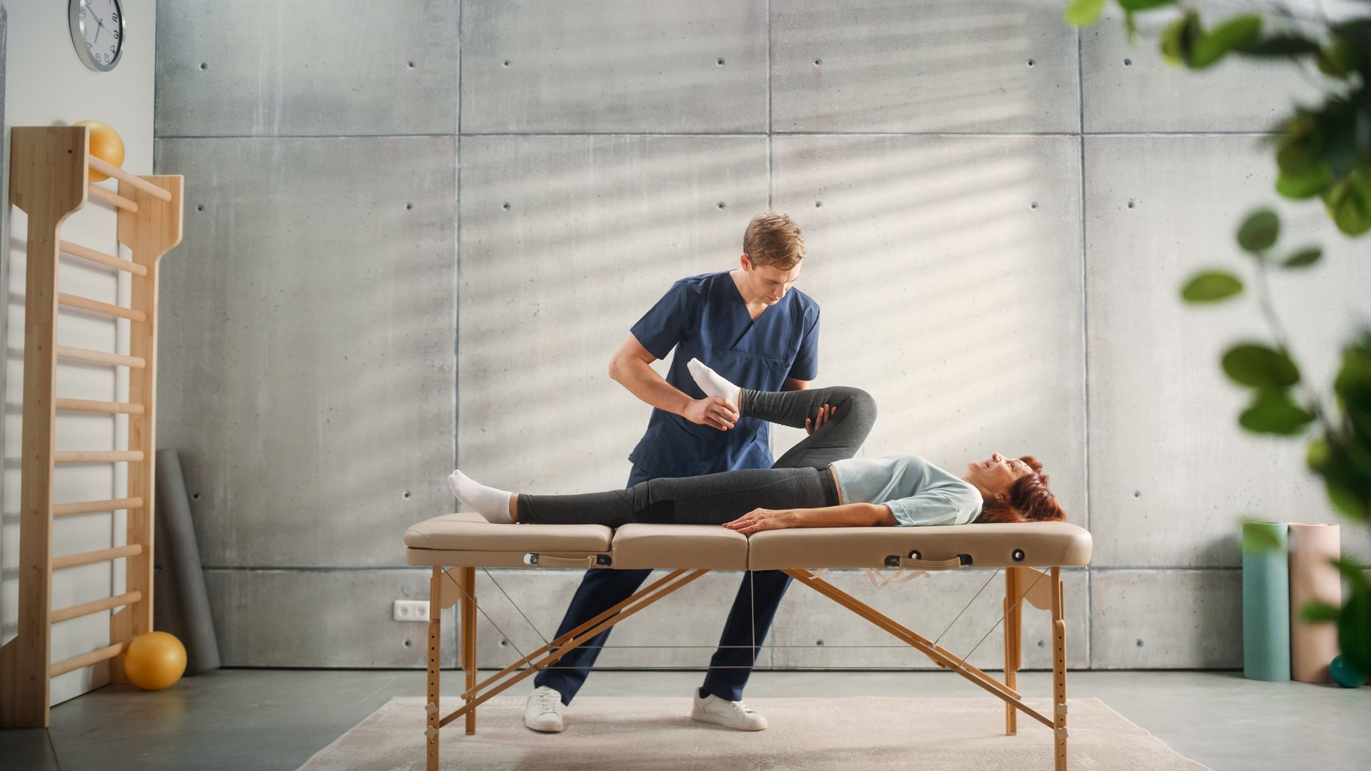 Physical therapist stretching a patient on a treatment table in a bright therapy room