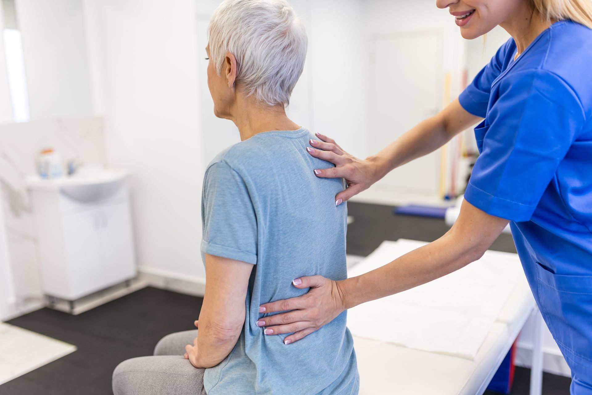 Therapist helping a seated patient with back and shoulder massage in a clinic exam room