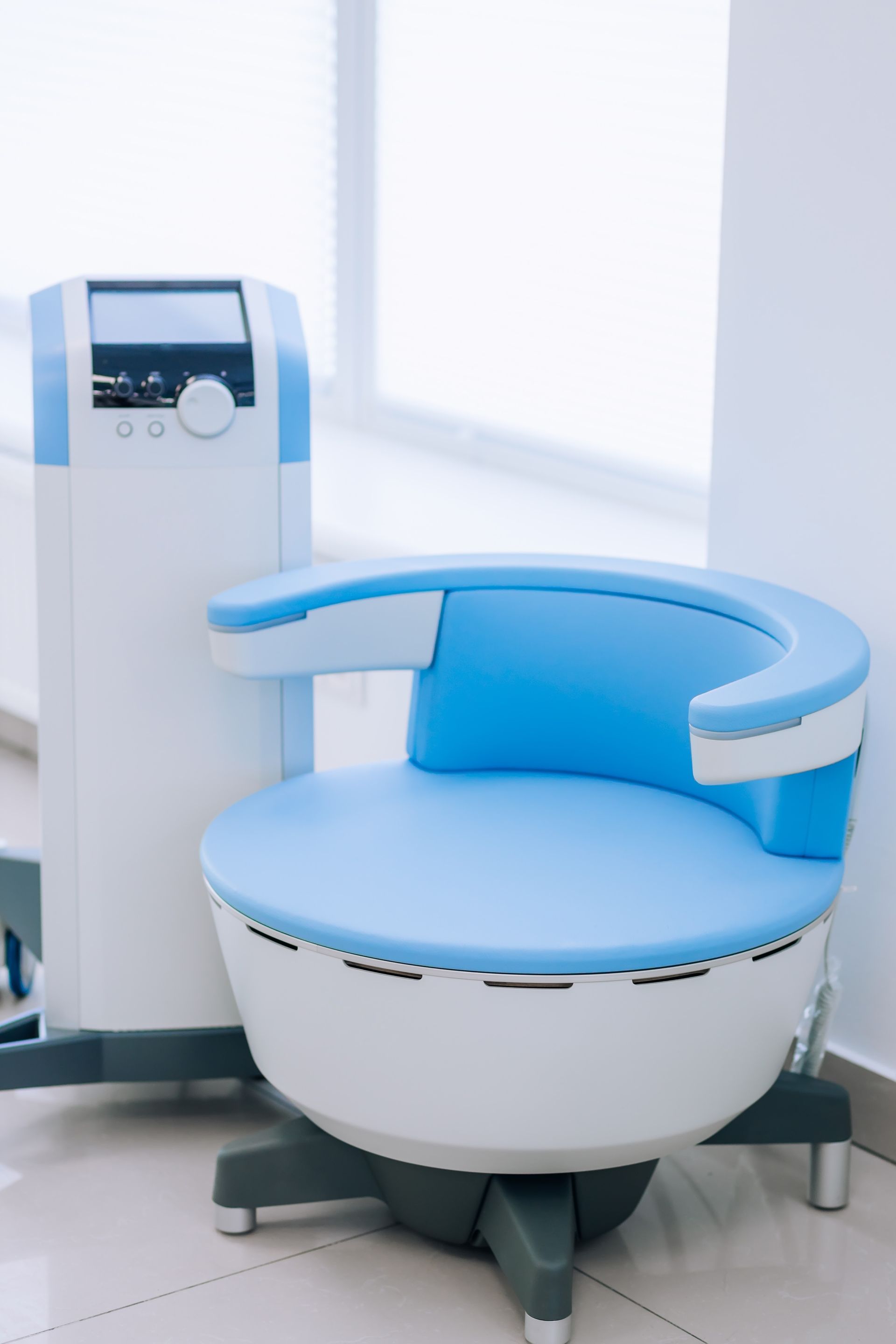 Blue-and-white medical treatment chair beside a control unit in a bright clinic room
