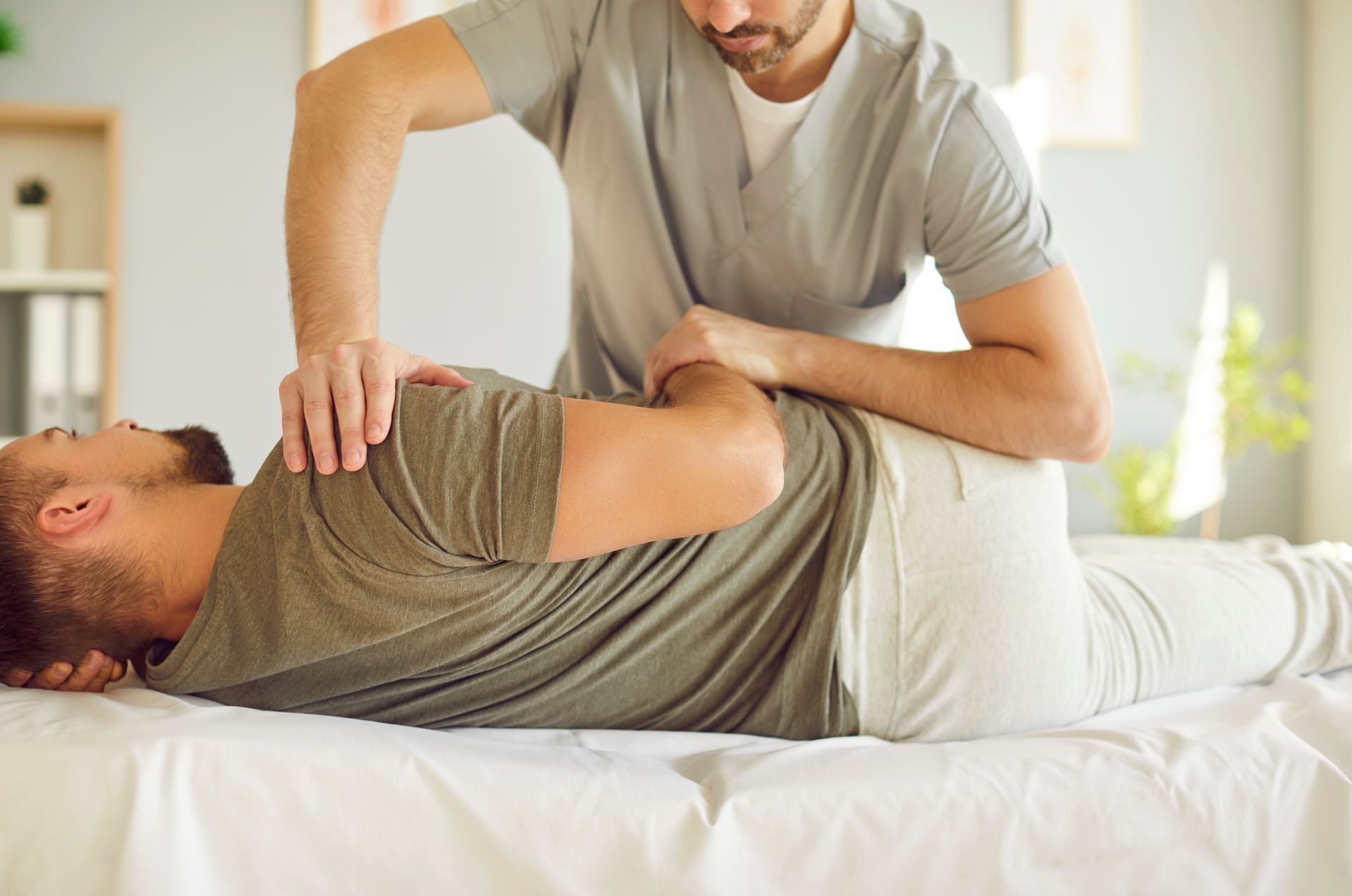 Therapist stretching a man’s back on a massage table in a bright clinic room