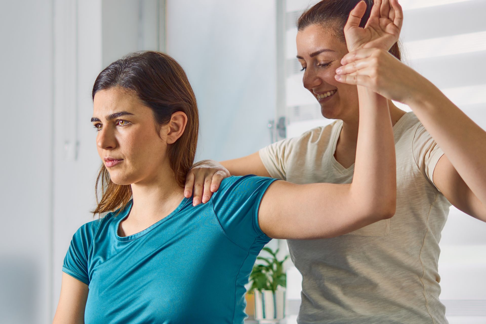 Woman doing arm stretch with trainer assisting in a bright room