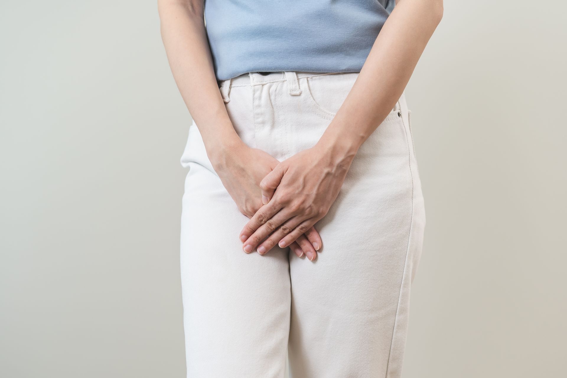 Person holding their lower abdomen in white pants against a plain background