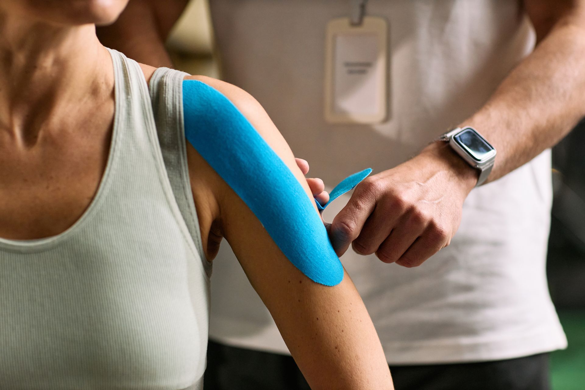 Healthcare worker applying blue kinesiology tape to a person's upper arm