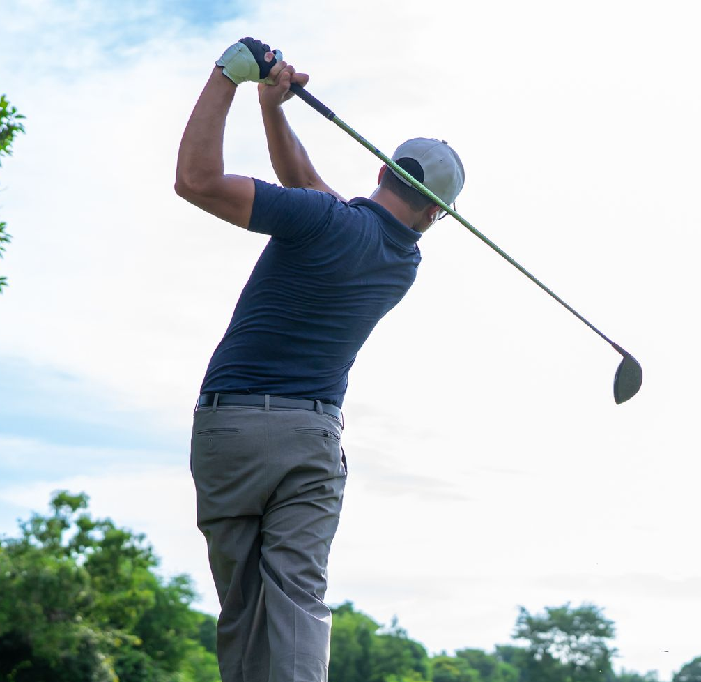Golfer in blue shirt and gray cap swinging a golf club outdoors on a green course