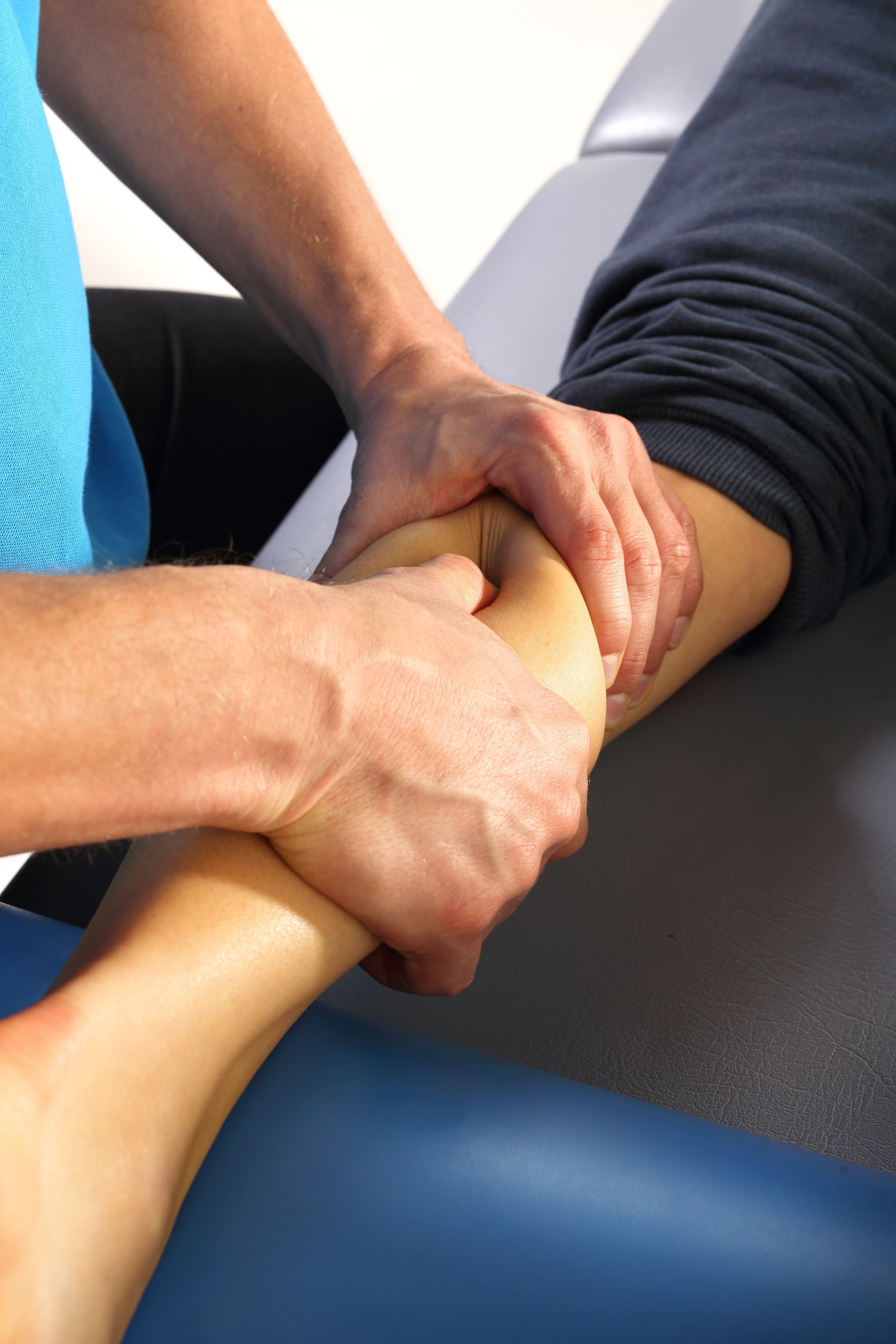 Hands performing a massage or therapy on a person's lower leg and ankle on a treatment table.