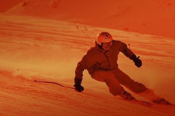 Skier carving down a snowy slope under orange light, kicking up snow spray