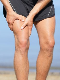 Person holding an injured knee on a sandy beach.