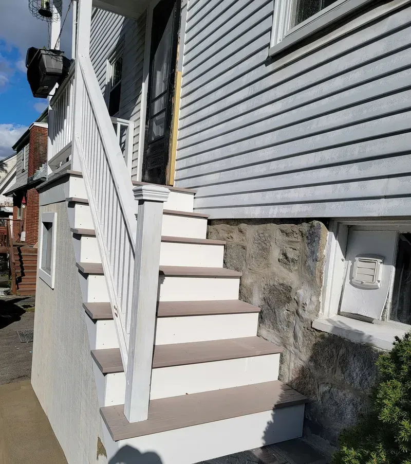 Exterior stairs leading to a doorway, painted white and brown against a gray building with stone foundation.
