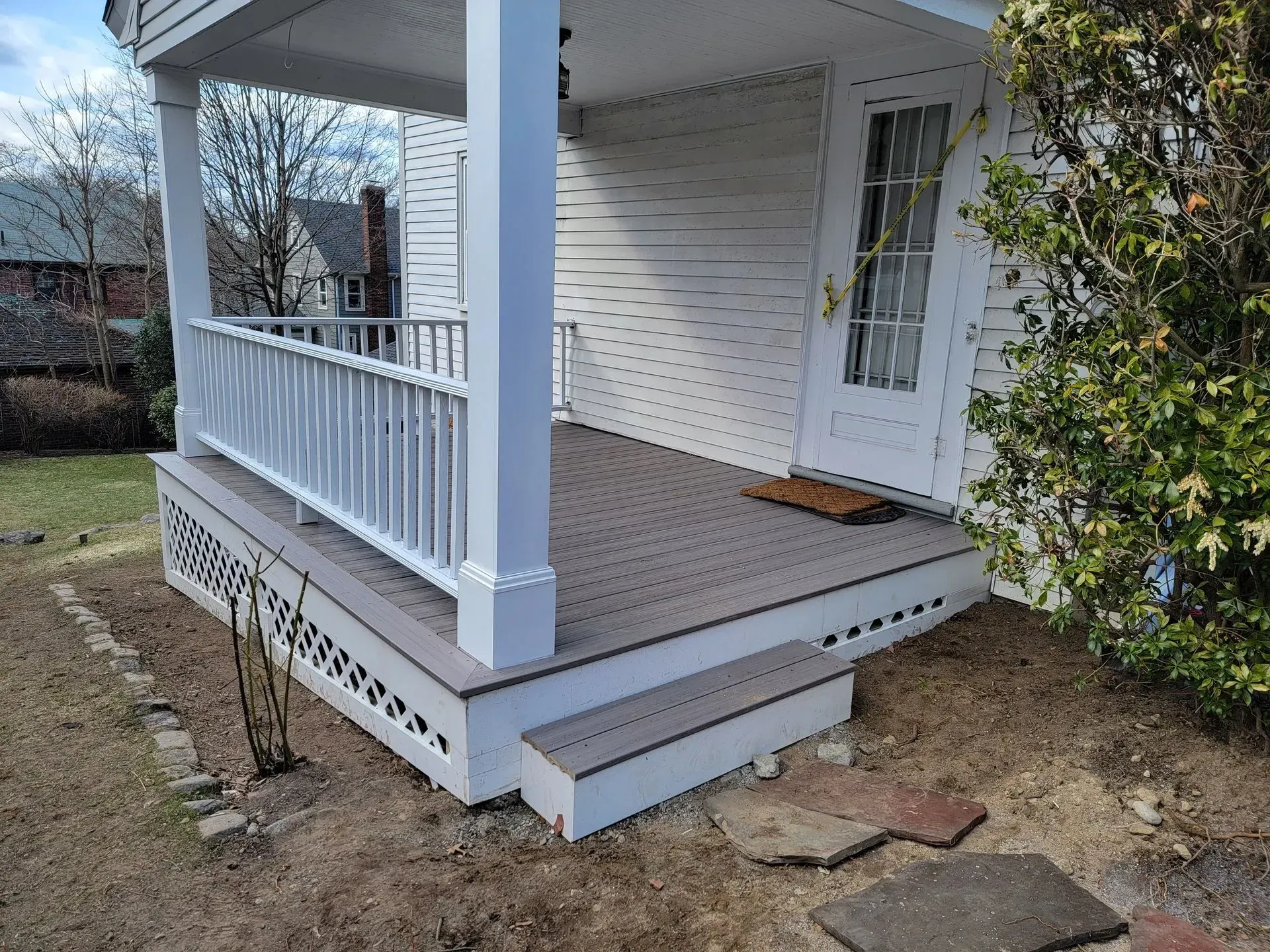 White house with porch, gray deck, steps, and railing.