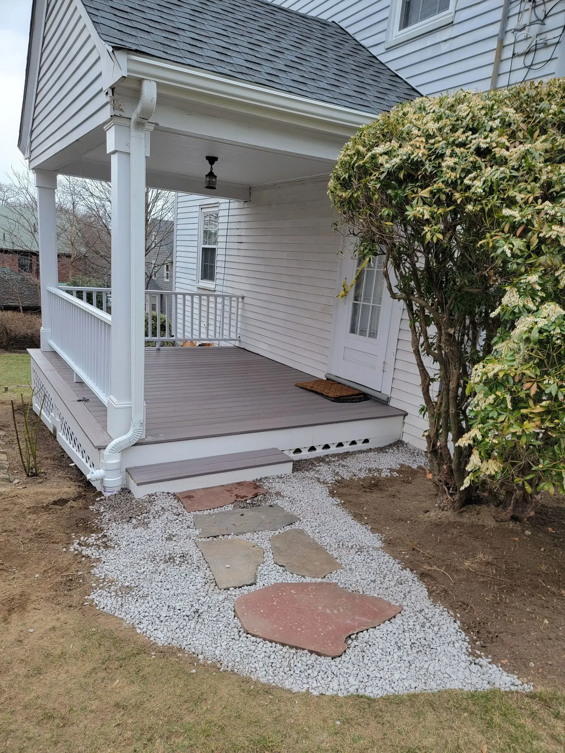 White house porch with stone path leading to it, surrounded by gravel and bushes.