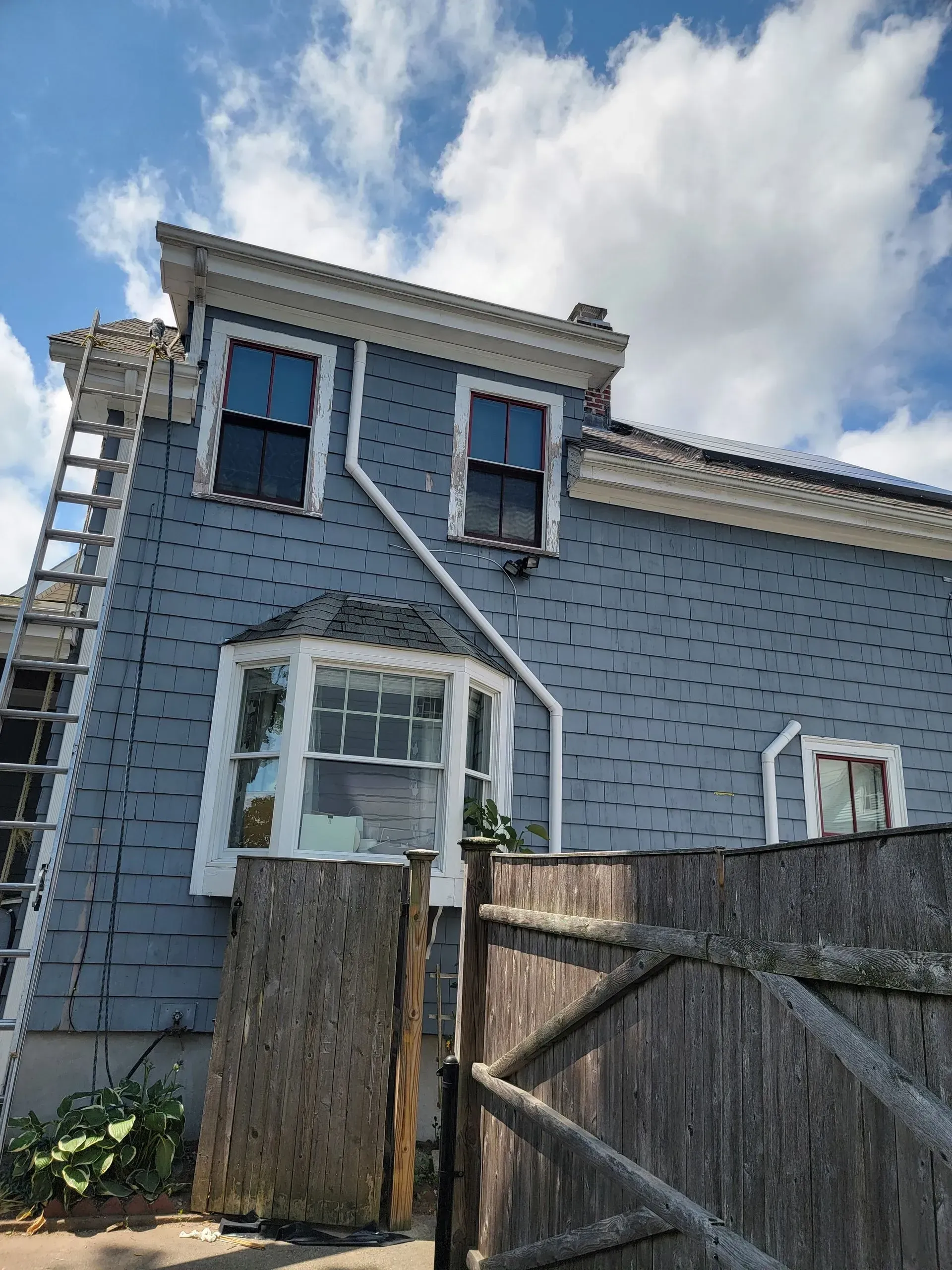 Blue house with white trim and a wooden fence; a ladder leans against the side.