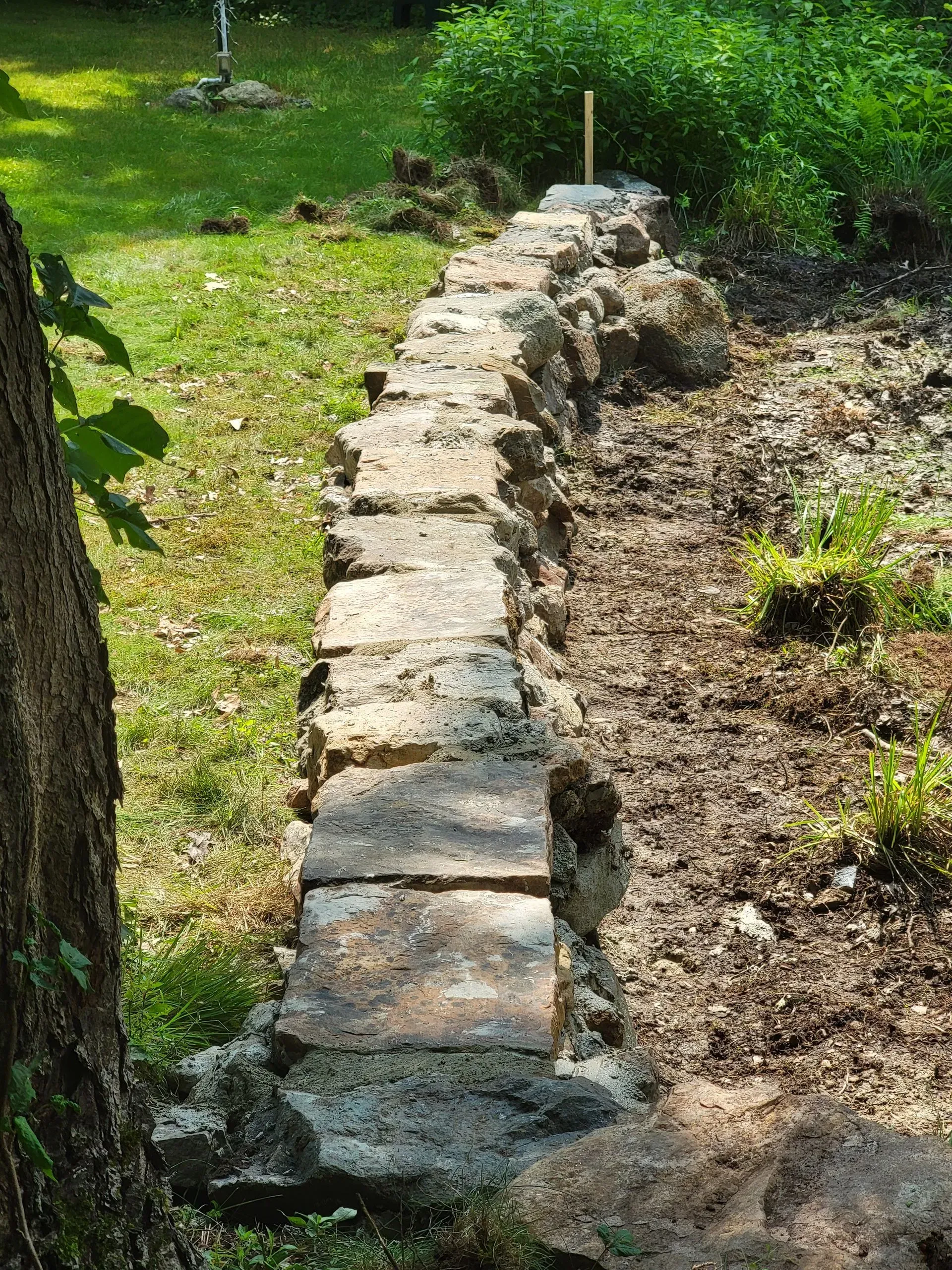 Stone retaining wall in a garden setting, with grass and soil.