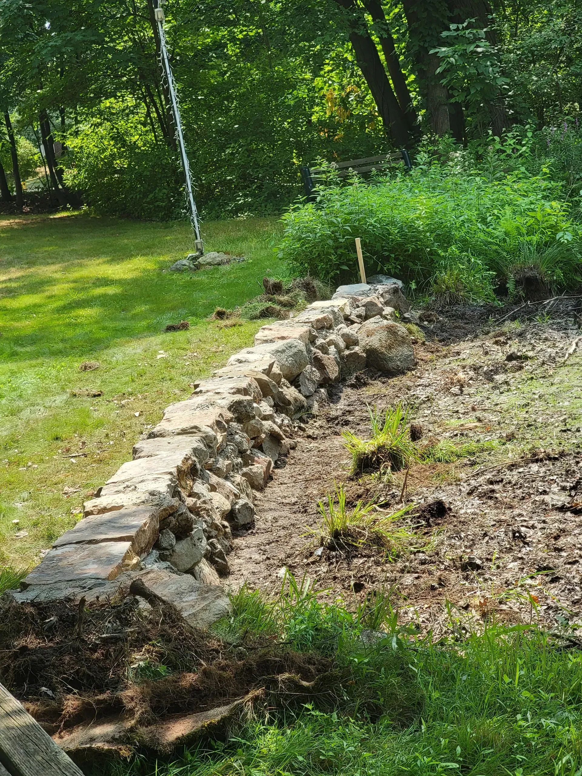 Stone retaining wall on a hillside; grass and trees in background.