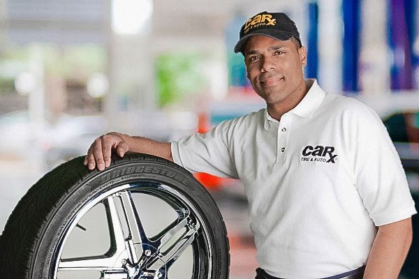 Man in polo shirt and cap leans on a tire; shop interior.