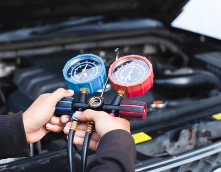 Mechanic holding blue and red gauges connected to a car engine for air conditioning service