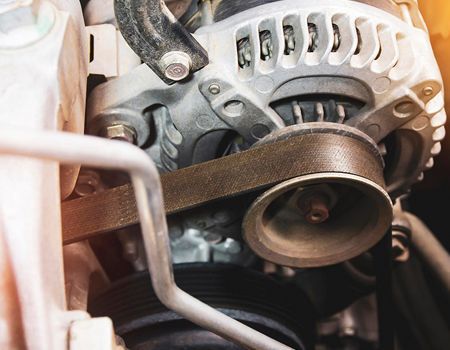 Close-up of a car engine alternator and belt system with metal pulleys and wiring.
