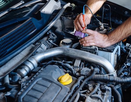 Mechanic working under open car hood with a tool in the engine bay