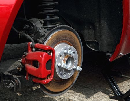 Close-up of a red car’s exposed wheel brake assembly with rotor and caliper removed or serviced