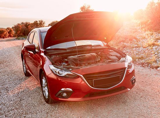 Red car with hood open on a roadside at sunset