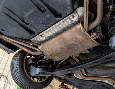 Undercarriage of a car with a rusty metal skid plate and visible front wheel