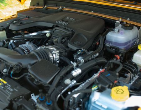 Car engine bay with a black cover, visible hoses, belts, and a purple coolant reservoir