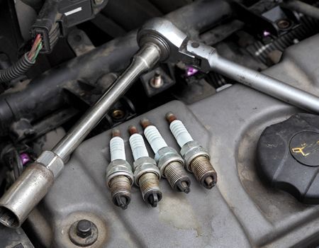 Mechanic’s tools and four spark plugs on an engine cover in a car bay