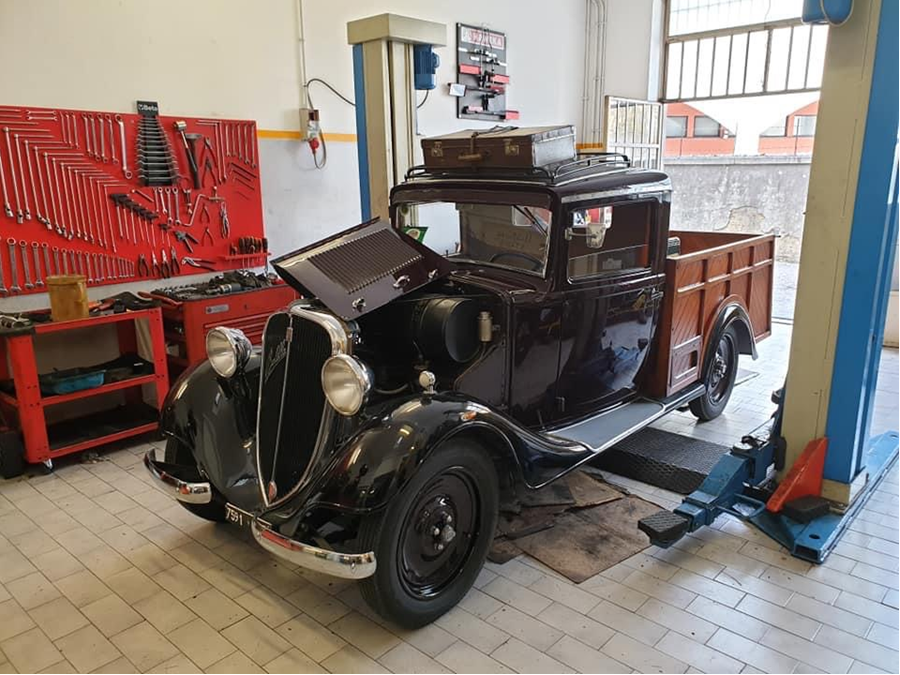 Auto nera d'epoca su un ponte sollevatore in un garage, con attrezzi e attrezzature nelle vicinanze.