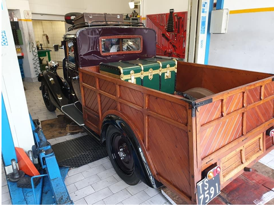 Pick-up d'epoca in un garage, con pianale di carico in legno e cassone portaoggetti verde sul retro.