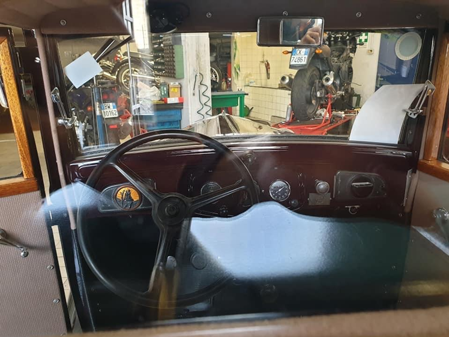 Interno di un'auto d'epoca con volante e cruscotto neri, visto attraverso il parabrezza in un garage.