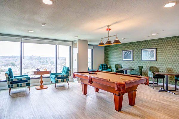 Pool table in a room with chairs, a small table, and a large window overlooking trees.