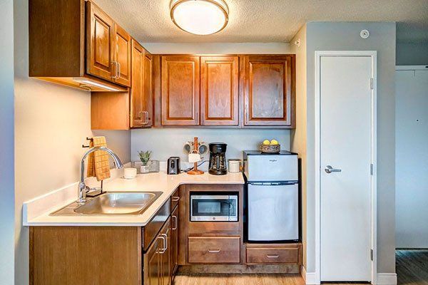 Small kitchen with wooden cabinets, microwave, refrigerator, and sink.