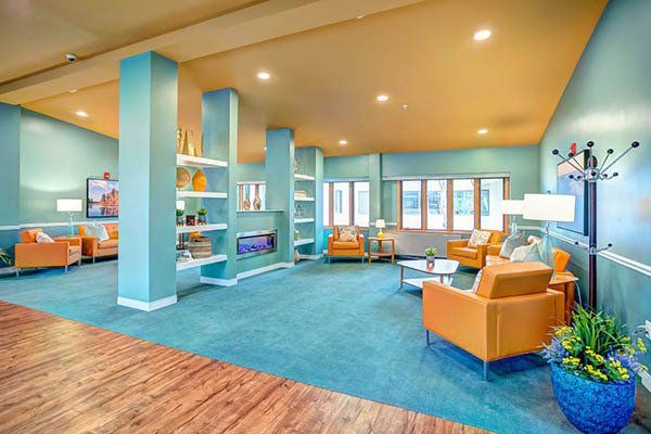 Spacious, teal-carpeted lounge area with orange furniture, teal pillars, and a yellow-orange ceiling.