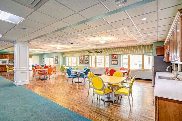 Dining area with colorful tables and chairs, wood floors, and windows.