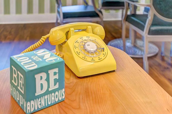 Yellow rotary phone and turquoise block with inspirational words on a wooden table.
